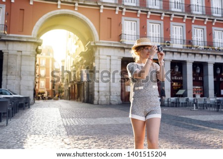 curly white girl tourist in a hat with a camera smiling photographs and exploring the city