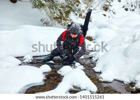 Professional photogtapher taking photos of a frozen river on wintertime in the mountains