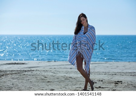 The girl stand on the beach and posing on camera. A beach towel blowing in the wind in her hands. Beach towel flying with the wind, summer beach - image