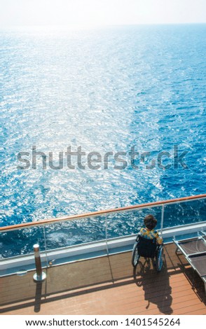 Disabled woman in a wheelchair on the deck of a cruise ship looking at the bright sunlight, the concept of travel accessibility for disabled Royalty-Free Stock Photo #1401545264