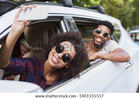 Young happy afro man and woman in sunglasses making selfie traveling in car with friends