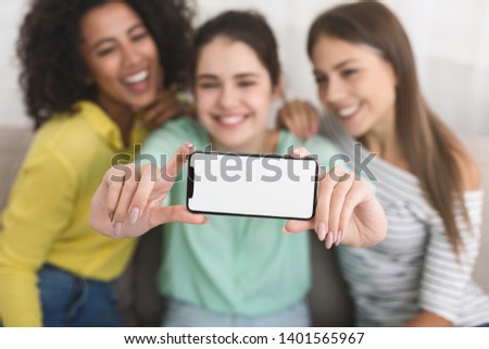 Diverse girls making photos on smartphone at home, phone with blank screen