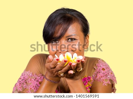 isolated portrait of beautiful and happy middle aged Indonesian Balinese woman in traditional ceremony dress smiling and holding flower offering in her hands in welcome to Bali Hindu religion 