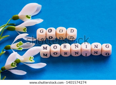 good morning written in wooden letters on a blue background with the first flowers of snowdrops