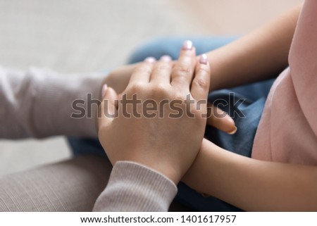 Close up of mom support child hold little daughter hands show love and care, mother or nanny touch comfort small girl child make peace or reconcile after fight, parent and kid tender moment together