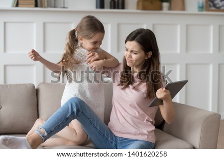 Preschooler little girl child sit on couch with parent behave bad demand tablet battle with young mom, small child fight with elder sister or nanny for taking pad playing games or watching cartoons