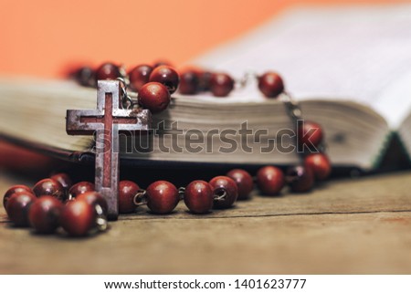 Old red Beads and crucifix on a Bible. Beautiful Coral Orange background. Religion concept.