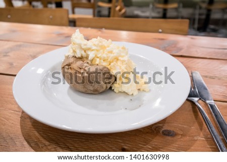Egg Mayonnaise filling on a baked jacket potatoe on white plate with cutlery on a wooden table in a cafe.