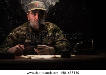 The evil dictator sitting on table. Angry communist general sitting at headquarter or Cuban commander in dark room. Studio decoration