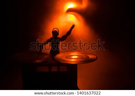 Dj club concept. DJ mixing, and Scratching in a Night Club. Man silhouette on vinyl turntable, strobe lights and fog on background. Creative artwork decoration with toy. Selective focus