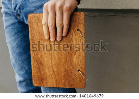 A book with a wooden cover in the hands of a guy. The guy holds a notebook with a wooden cover. Closeup top view of female hands holding brown canvas photo book