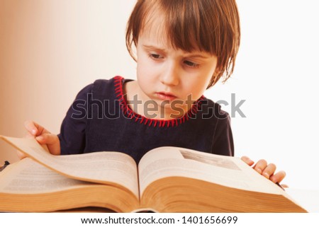 Little cute child girl watching a book as symbol of science, education and knowledge