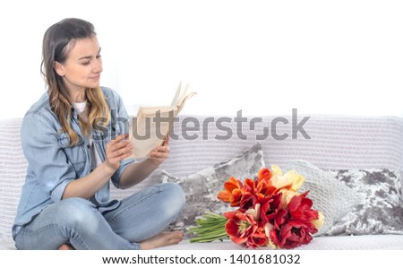 Young girl reading a book on the couch in the living room , next to a large bouquet of tulips .
