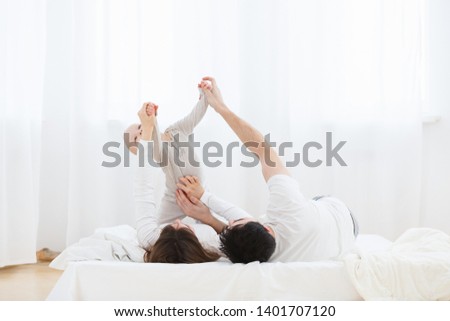 Portrait of young parents playing with little one-year old baby boy on bed indoors. Smiling baby raised hands up from pleasure. morning exercises for the baby with parents