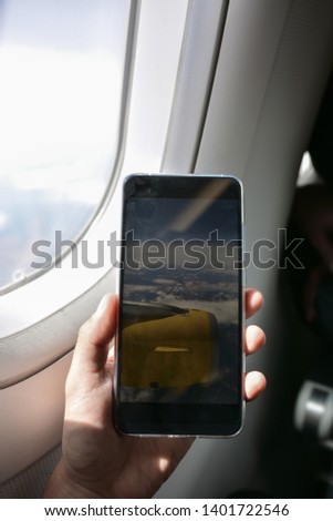 Smartphone taking pictures from the window of the plane, while flying above the clouds