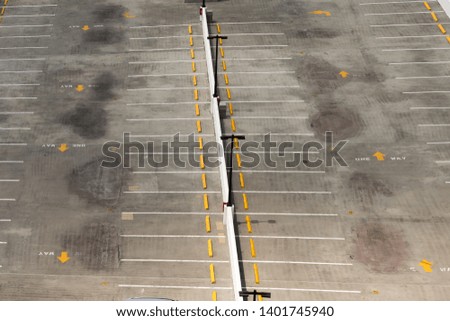 An empty parking lot at the top of a parking garage. It has yellow directional arrows and white lines spaces.