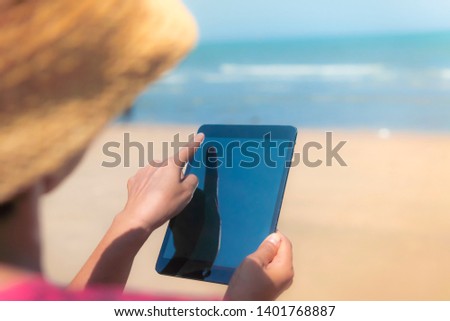 Women are using the tablet with internet. On the summer beach