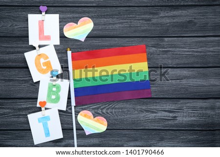Paper with abbreviation LGBT and rainbow flag on black wooden table