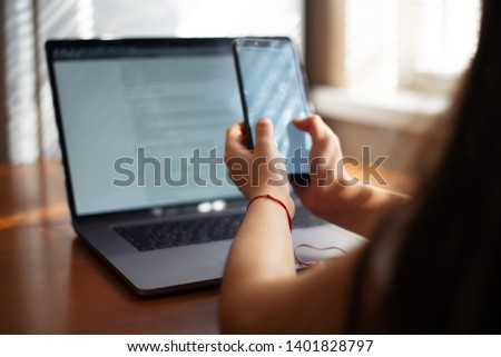 Smartphone in hands over laptop background, on wooden desk