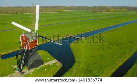 Aerial view of a old dutch traditional windmill on the rural countryside in The Netherlands with a dike, canals. railway. bridge and a road.