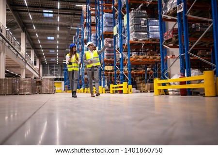 Warehouse managers walking in a large storage department controlling distribution to the market. Royalty-Free Stock Photo #1401860750