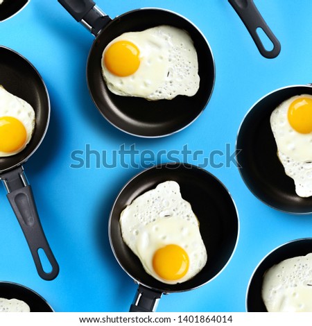 Creative food pattern with fried eggs on pans over blue background. Top view. Creative pattern in minimal style. Flat lay. Square crop.