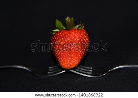 Red strawberry on forks against a black background