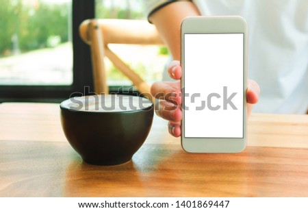Mockup image of hands holding white mobile phone with blank white screen with Modern coffee shop with coffee 