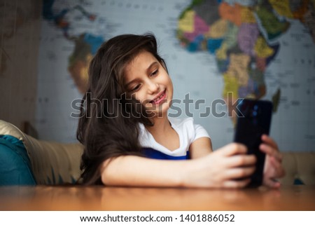 Portrait of cheerful modern children girl with smartphone in hands, on background of world map