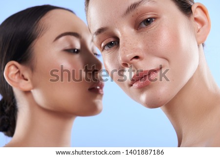 Low angle of young pretty Asian and Caucasian ladies with different types of skin standing near each other and looking at camera in studio. Beauty, facial treatment and spa concept Royalty-Free Stock Photo #1401887186