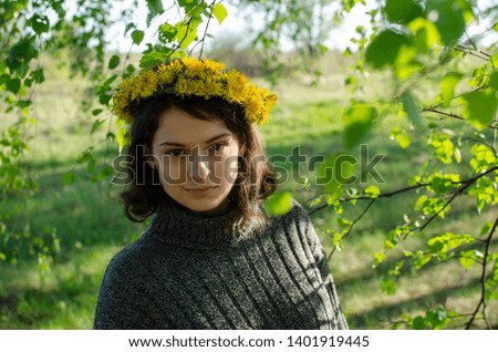 Young beautiful brunette girl with a wreath of dandelions on her head in the rays of the sunset