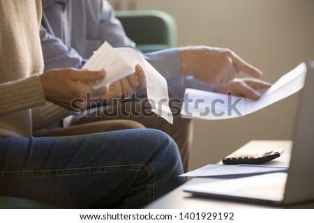 Elderly spouses sitting on couch at home planning budget check bills cheques, computer, documents and calculator on coffee table, close up cropped concept image, couple manage family expenses concept Royalty-Free Stock Photo #1401929192