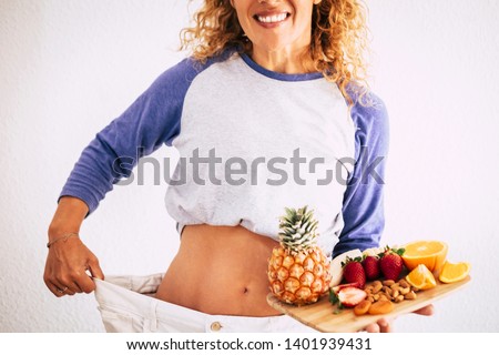 beautiful woman showing her old big pantalon after losing weight ah home - fitness at home and working to stay better with yourself - eating good with a lot of fruits in her hands like pineapple Royalty-Free Stock Photo #1401939431