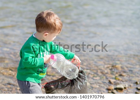 Save environment concept, a little boy collecting garbage and plastic bottles on the beach to dumped into the trash Royalty-Free Stock Photo #1401970796