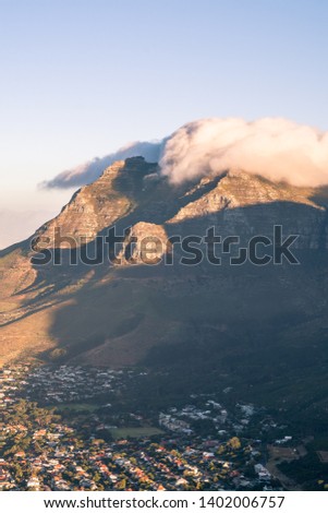 Portrait photo of a rocky mountain with clouds partially covering the peak at sunset. Pictured : Devil's Peak, shot from Lion's Head in Cape Town, South Africa. 