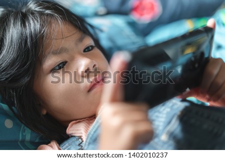 Little cute girl playing games on her smartphone on morning time after wake up, Selective focus, Children’s Smartphone Addiction problem.