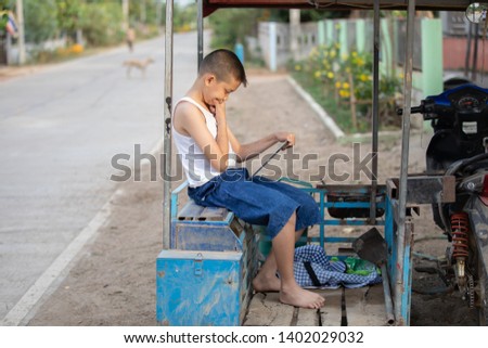 Young cute boy using tablet and he is touching the screen with happy smile. He is sitting on the old vehicle with countryside background. he has a lot of expression on his face such as happy and think