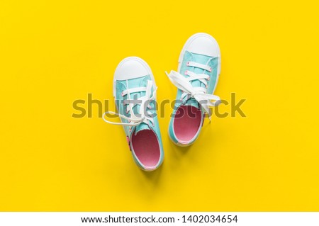 New turquoise sneakers on yellow background with copy space. White blue pink cross laces