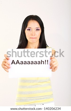 Surprised young woman holds inscription "ah" on grey background