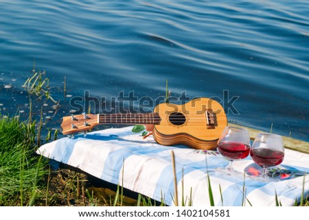 hawaiian guitar and two red wine glasses, picnic on the lake and summer vacation concept