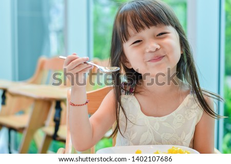 Little asian child girl having breakfast at the morning with a happy smiling face Royalty-Free Stock Photo #1402107686