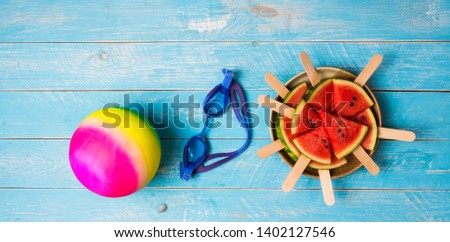 Watermelon cut into pieces Plugged in with a stick, making it like ice cream, stacked in a side dish with swimming goggles and ball for water activities. Is an item for the summer time to cool off .