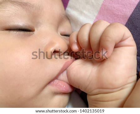 sleepy six months baby sucks thumb  Royalty-Free Stock Photo #1402135019