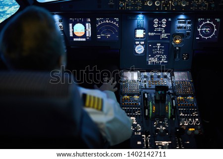 Rear view of unrecognizable pilot sitting at control panel with radar devices and flight system buttons and flying plane on autopilot Royalty-Free Stock Photo #1402142711