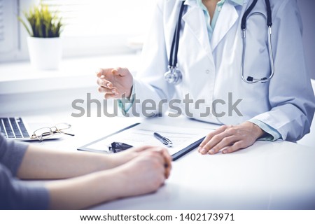 Doctor and  female patient sitting at the desk and talking  in clinic near window. Medicine and health care concept. Green is main color Royalty-Free Stock Photo #1402173971