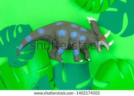 funny dinosaur toy on green background with green paper cut tropical leaves