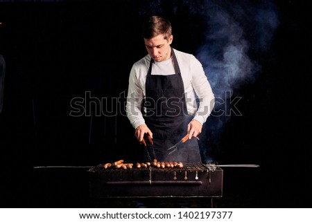 the guy is grilling sausages in an apron
