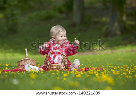little red hood toddler seated in grass with buttercups