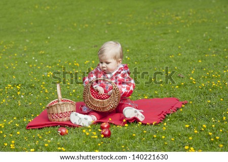 little red hood toddler seated in grass with buttercups