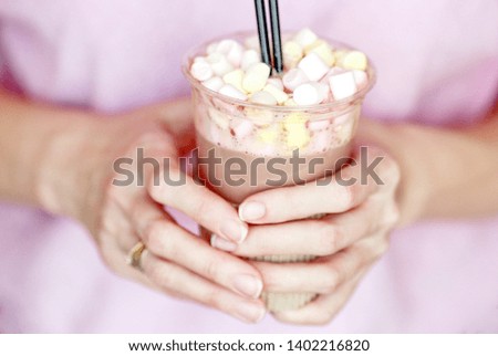 marshmallow cocoa in a disposable cup with two tubes in the hand of a woman